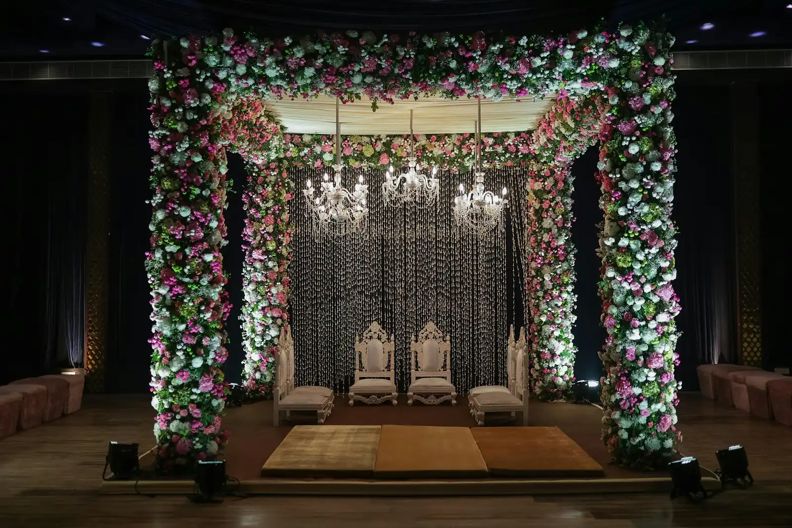 Luxurious floral mandap adorned with chandeliers in a palace courtyard.