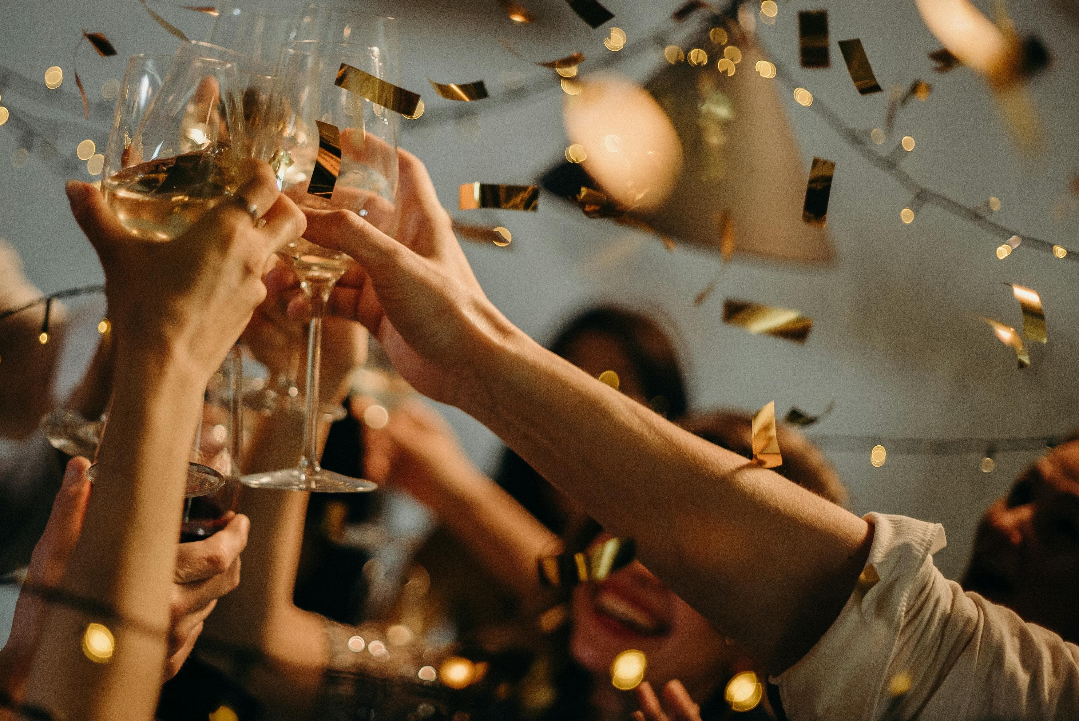 A lively indoor party scene with people toasting champagne glasses amid confetti and warm lights:contentReference[oaicite:1]{index=1}.